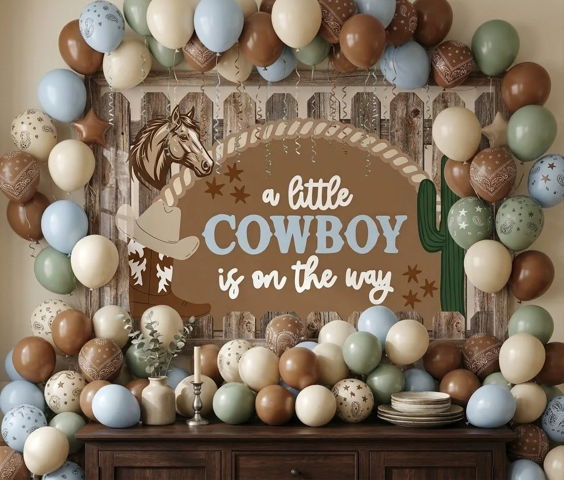 An earth-tone balloon frame in tan, sage, chocolate and pale blue around a hand-painted “a little cowboy is on the way” sign with a horse and cactus
