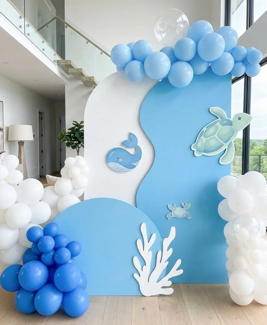 Blue and white balloon garlands over layered wave-shaped panels with painted whale, turtle and coral cut-outs for an under-the-sea party