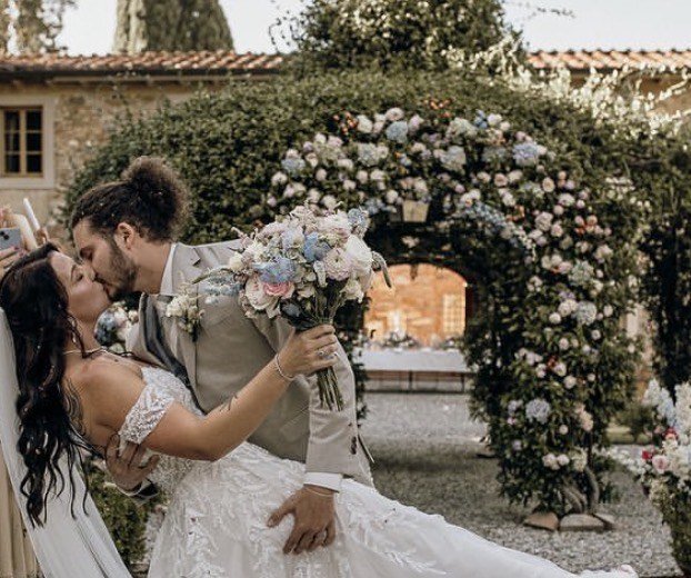 A couple kiss beneath a rose-covered arch in the courtyard of a stone villa