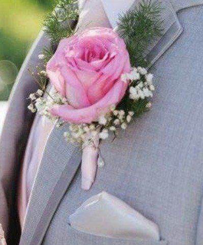A single pink rose boutonnière with baby's breath and fern on a grey suit lapel